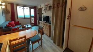 A cozy living room with a sofa, a dining table, and a TV. There is a kitchen area with a refrigerator and a cabinet. - 4th floor, view valley, balcony, tv, ski locker, 23m², Valfréjus (Valfréjus)