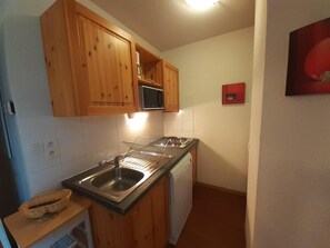 A compact kitchen with wooden cabinets, a microwave, a sink, and a dishwasher.