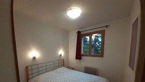 A bedroom with a bed, a window with curtains, and a wall-mounted light fixture. - 180m from ski lifts, floor -2, balcony, tv, ski locker, 32m², Valfréjus (Valfréjus)