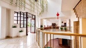 Un intérieur spacieux avec un sol en marbre, un ascenseur en verre et des plantes suspendues.