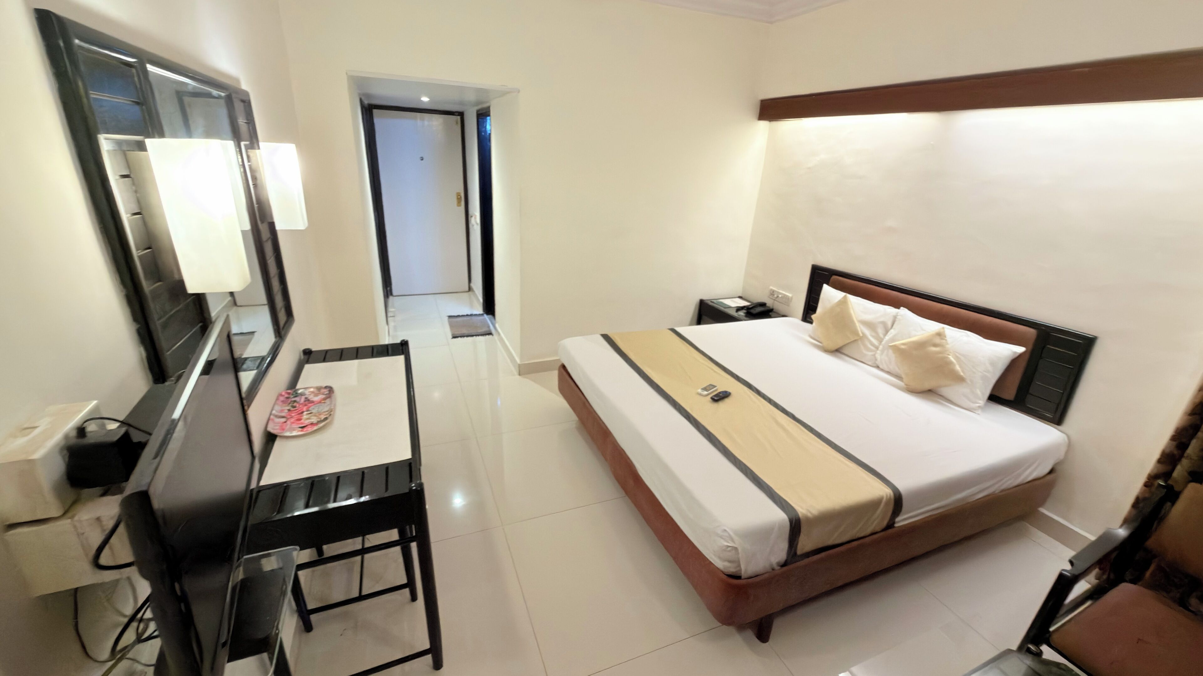 Una habitación de hotel con cama, escritorio, silla, espejo y mesita de noche.