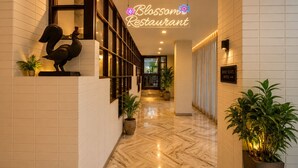 Un couloir doté d’un sol en marbre, de plantes en pot, d’une sculpture et d’un panneau lumineux néon indiquant le restaurant Blossom.