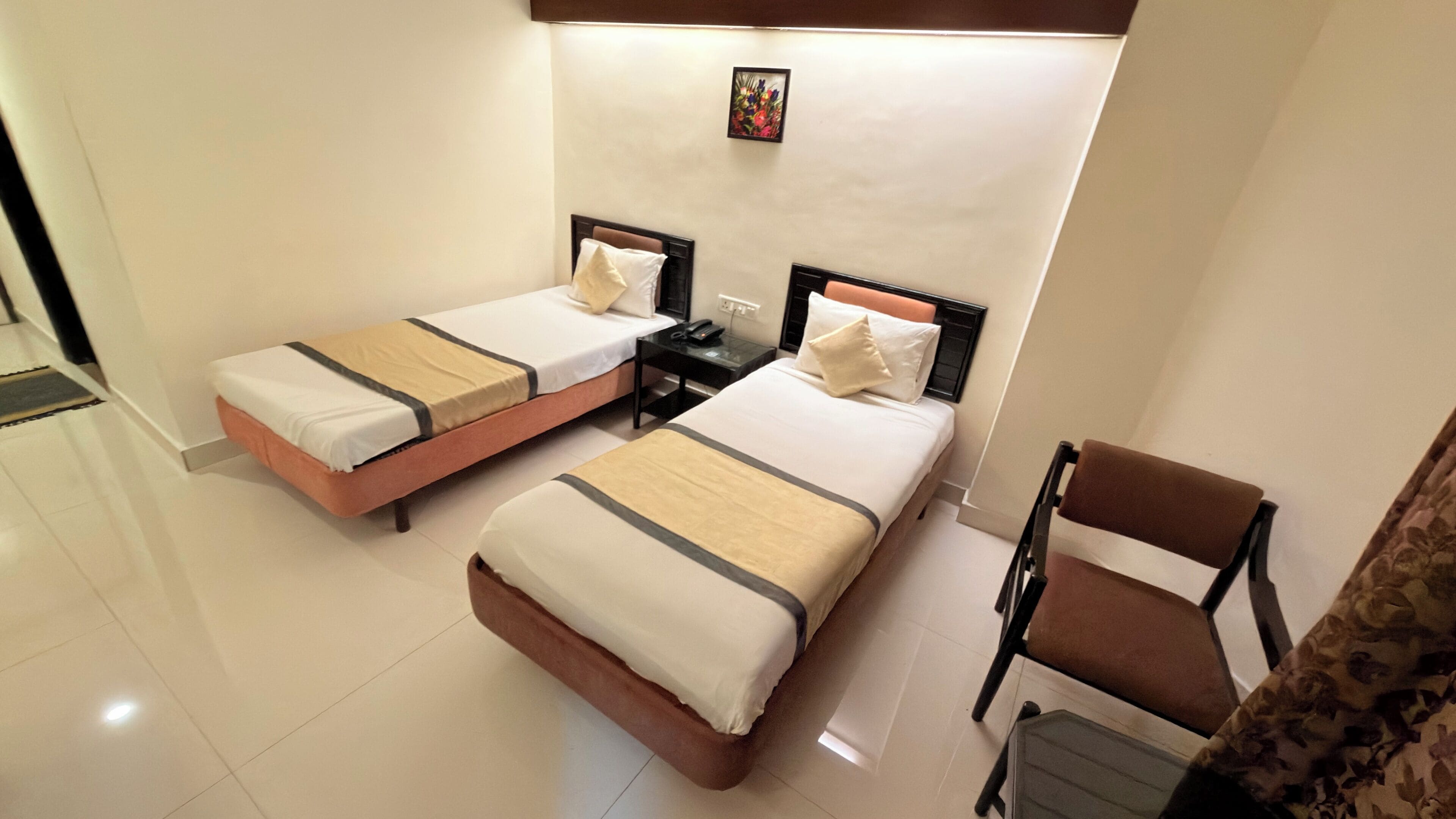 A hotel room with two single beds, a small table, a chair, and a nightstand with a phone.