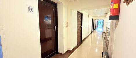 Pasillo de hotel con extintor montado en la pared, una puerta con código QR y un cartel con el número de habitación.