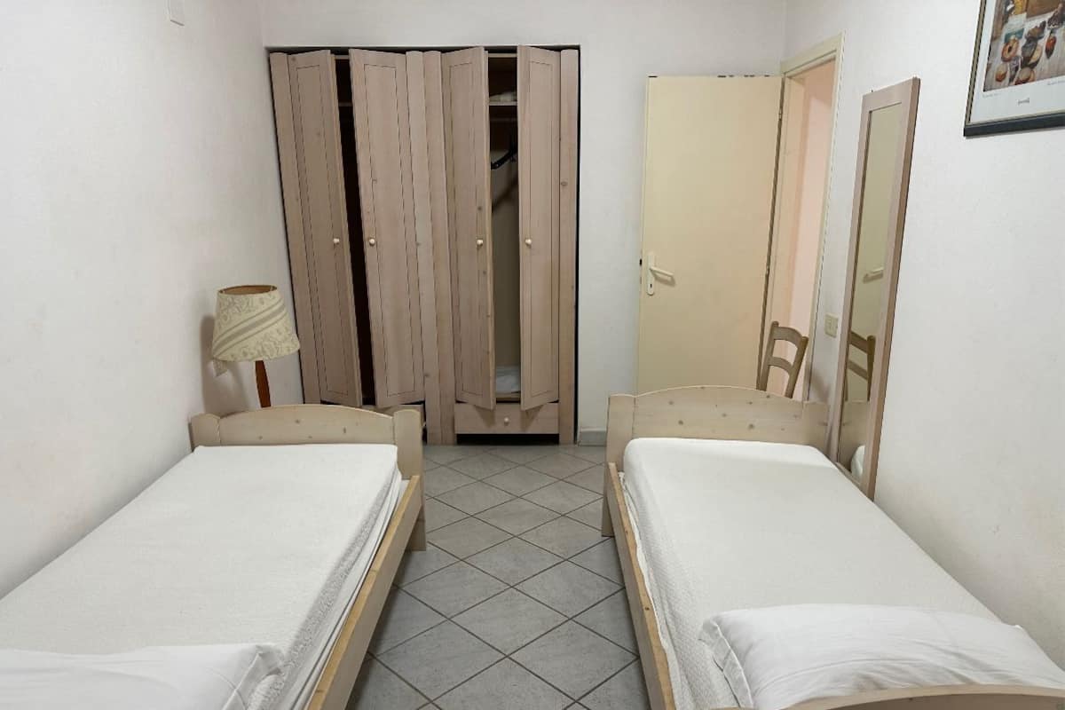 Une chambre avec deux lits simples, une armoire, un miroir et une lampe.