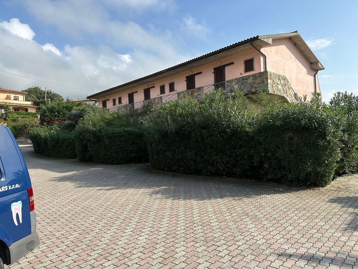 A building with a pink facade and stone base, surrounded by greenery.