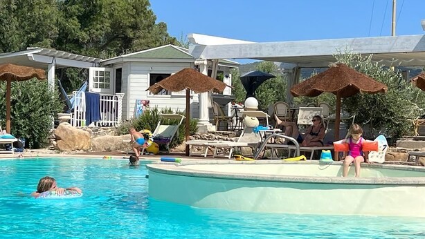 A swimming pool with lounge chairs and umbrellas, surrounded by a building with a white exterior and a covered area.