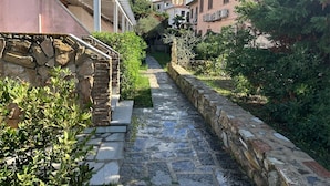 A narrow stone pathway flanked by buildings with stone walls and greenery.