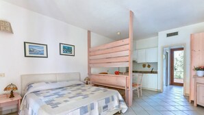 A bedroom with a bed, a desk, and a kitchenette.