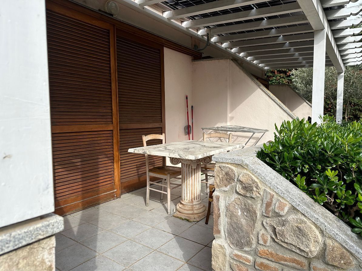 An outdoor patio with a stone wall, a table and chairs, and a wooden door.