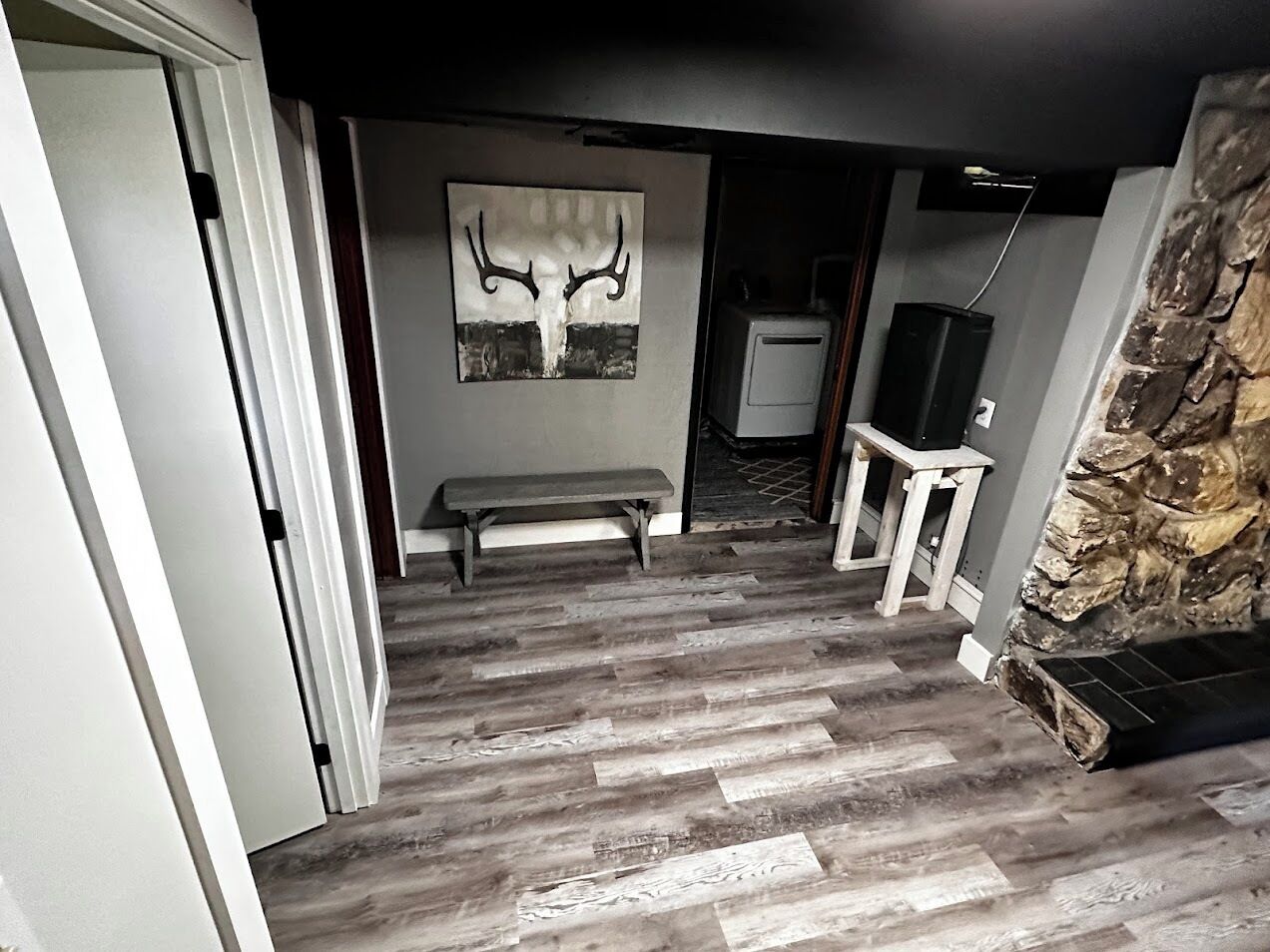 A room with a wooden floor, a bench, a stone wall, and a painting of antlers.
