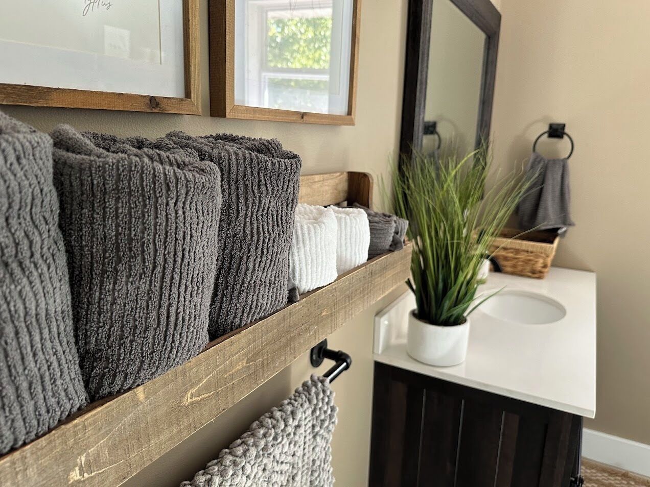 A bathroom with a wooden shelf holding towels, a potted plant, and a sink.