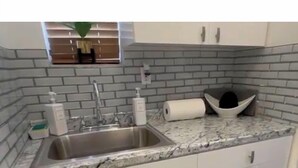 A kitchen with white cabinets, a granite countertop, a stainless steel sink, and a brick backsplash. - 🌴Luxe Oasis🌴 (Miami)
