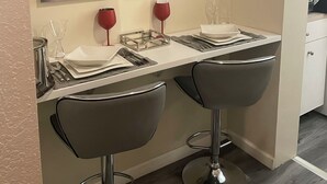 A modern kitchen with a large painting of a woman's face and a red rose, two bar stools, and a countertop with wine glasses and cutlery. - 🌴Luxe Oasis🌴 (Miami)