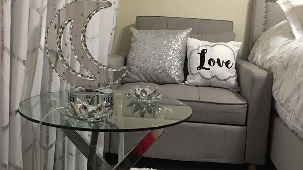 A modern bedroom with a glass table, a decorative moon sculpture, a sofa with a 'Love' pillow, and a white rug. - 🌴Luxe Oasis🌴 (Miami)