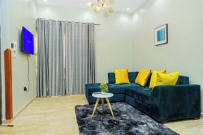 Un salon moderne avec un canapé de couleur turquoise, une petite table ronde et un rideau gris.