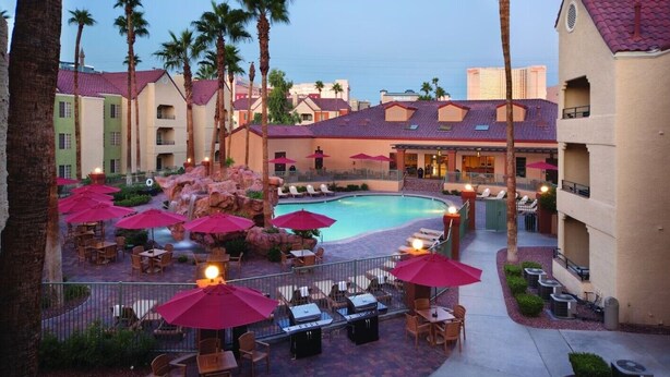 Un hotel con piscina, zona de estar al aire libre con sombrillas y palmeras.