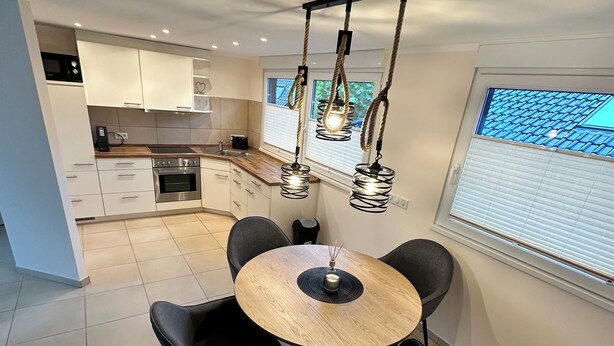A modern kitchen with white cabinets, a wooden countertop, and a round dining table with four chairs. - Vacation apartment / trade fair apartment - quietly located on the outskirts of Krefeld  (Krefeld)