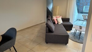 A modern living room with a grey sofa, a smaller grey armchair, and a round coffee table. A large window offers a view of a brick exterior. - Vacation apartment / trade fair apartment - quietly located on the outskirts of Krefeld  (Krefeld)
