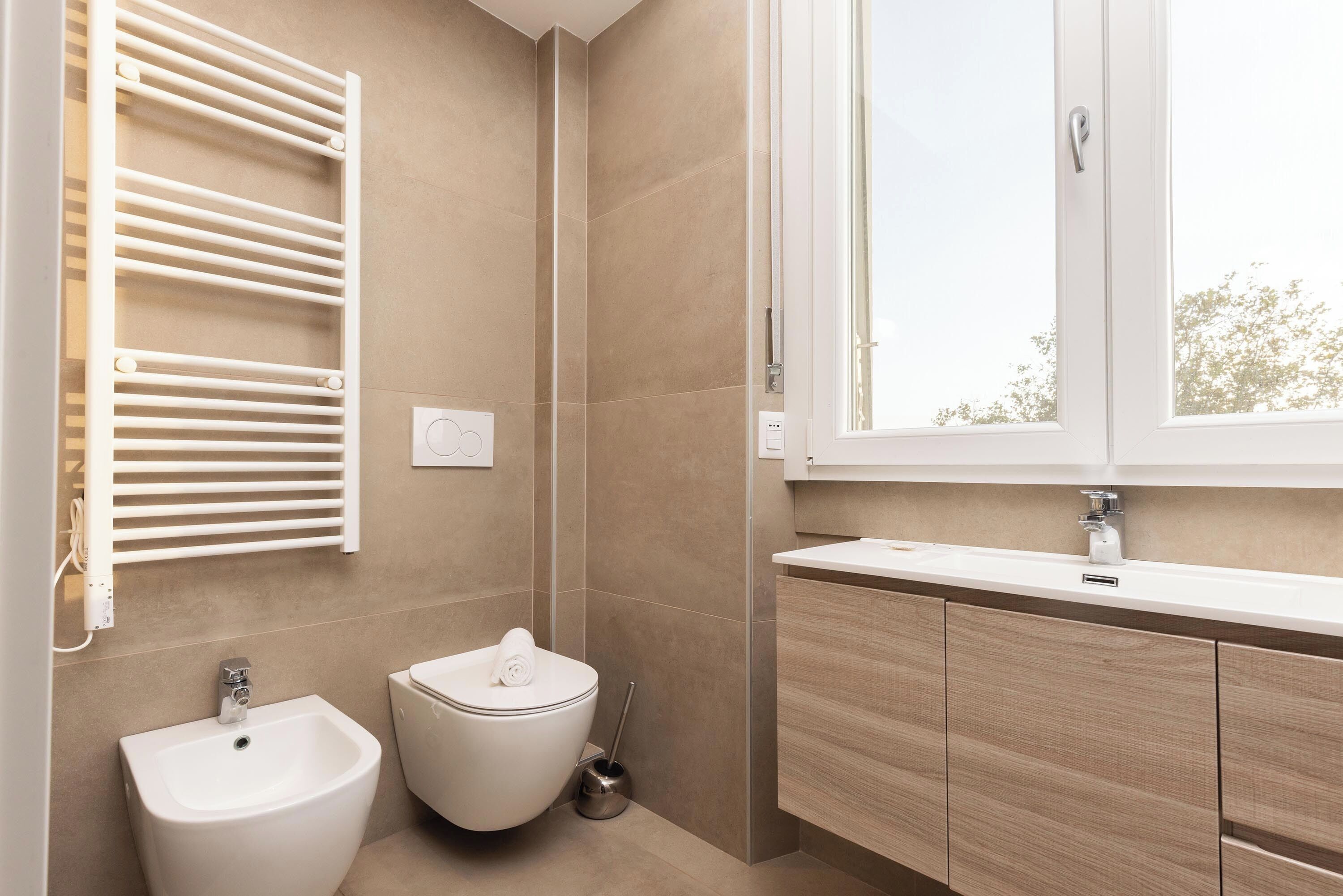 A modern bathroom with a bidet, toilet, and a window providing natural light.