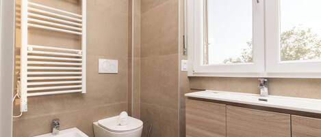 A modern bathroom with a bidet, toilet, and a window providing natural light.