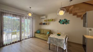 A spacious living area with a sofa, a dining table with a fruit bowl, and a TV on a wooden cabinet.