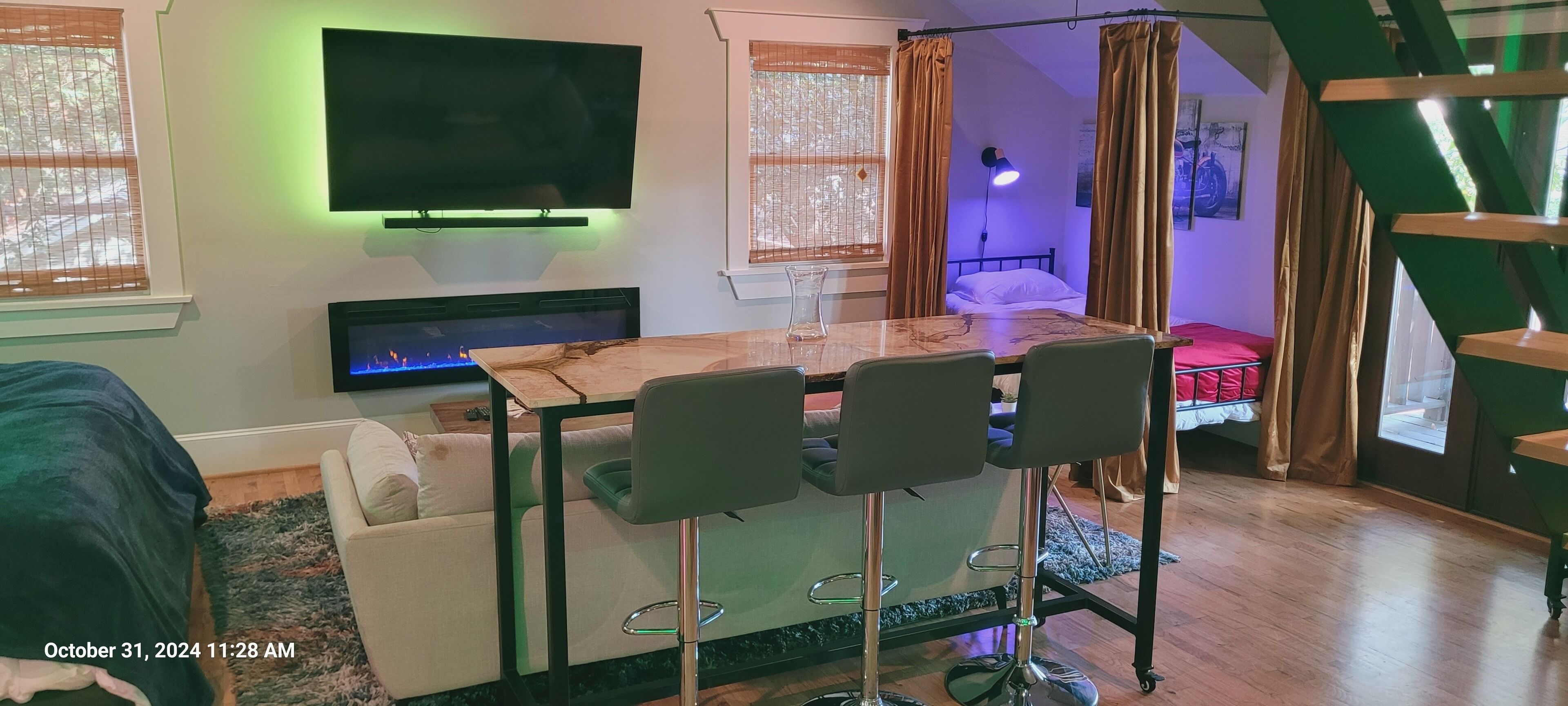 Een moderne kamer met een televisie, een open haard, een eettafel met stoelen, een bed en een trap.