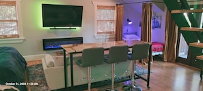 Una habitación moderna con televisión, chimenea, mesa de comedor con sillas, cama y escalera.