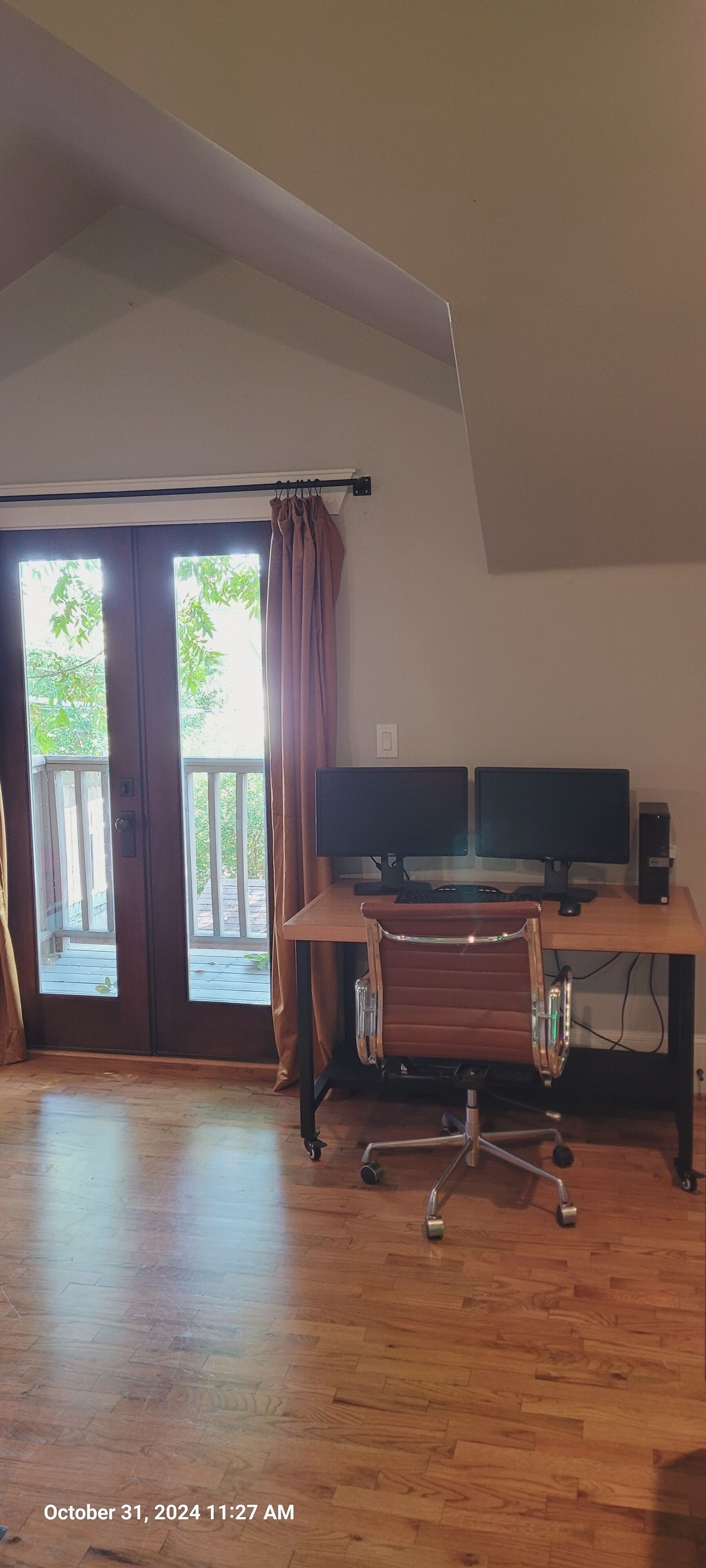 Ett rum med trägolv, ett skrivbord med två bildskärmar, en kontorsstol som kan vridas och en skjutdörr i glas som leder ut till ett utomhusområde.