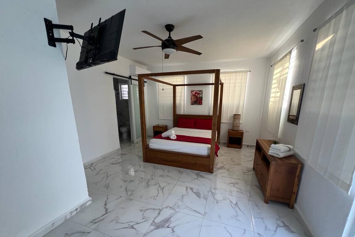 Ein geräumiges Schlafzimmer mit einem Himmelbett, einem Deckenventilator, einem an der Wand montierten Fernseher und einem Marmorboden.