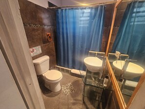 A bathroom with a toilet, a sink, a shower curtain, and a warning sign on the wall. - OMERO Ocean Park (San Juan)