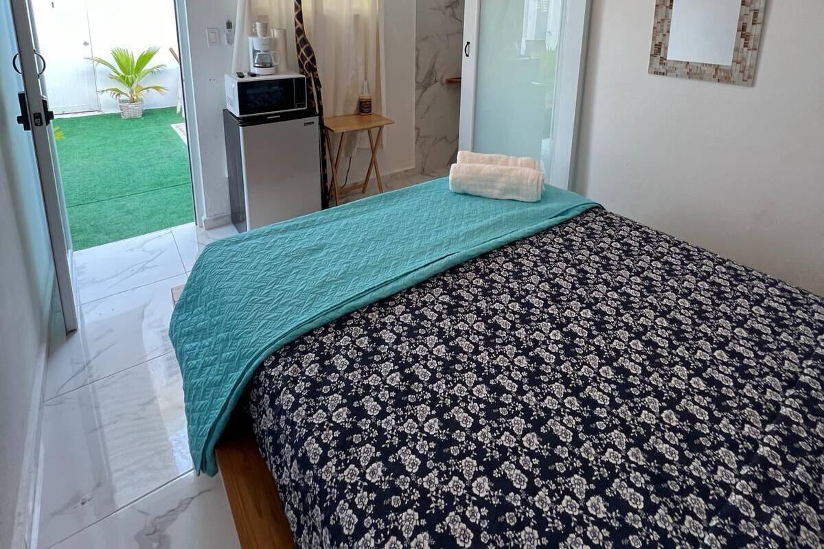 Ein Schlafzimmer mit einem Bett, einem Deckenventilator, einem Fernseher, einem kleinen Tisch, einem Spiegel und Blick ins Freie.