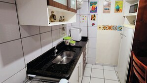 Cozinha compacta com pia, cafeteira e geladeira. Há itens decorativos e um calendário na parede.