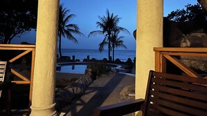 Un área de piscina con vista al océano, palmeras y un banco de madera.
