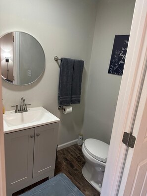 A bathroom with a sink, mirror, towel rack, toilet, and a poster on the wall.