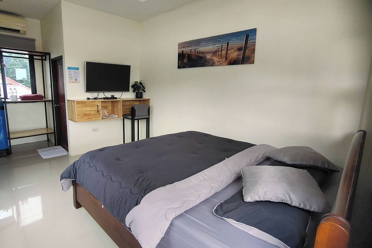 A bedroom with a bed, a desk, a chair, a TV, and a painting on the wall.