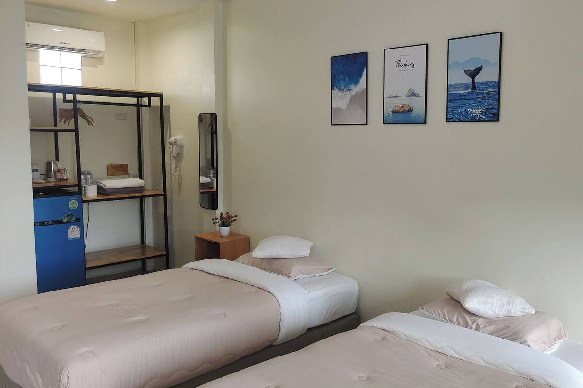 A hotel room with two beds, a desk with a computer, a mirror, and three framed pictures on the wall.