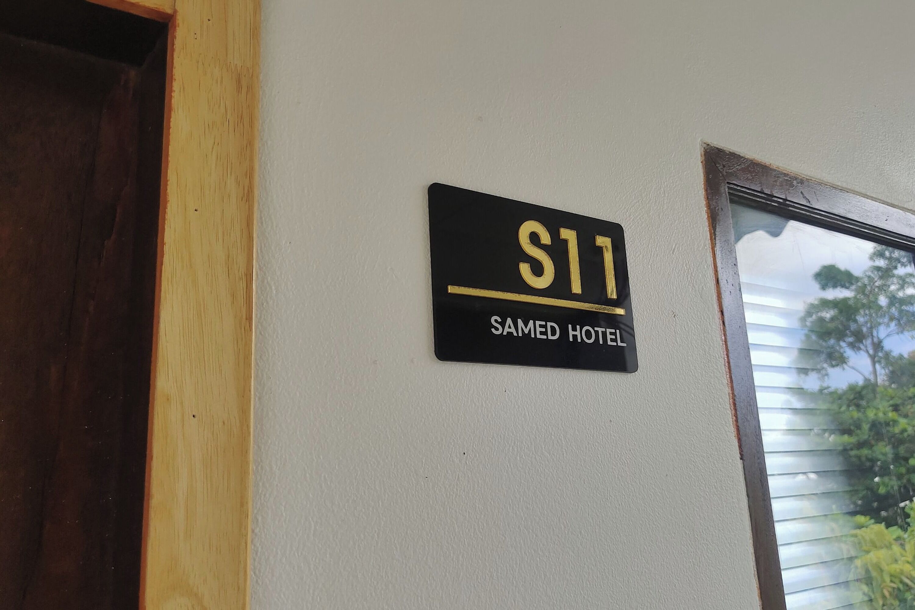 A black sign with gold lettering on a white wall, indicating the Samed Hotel.