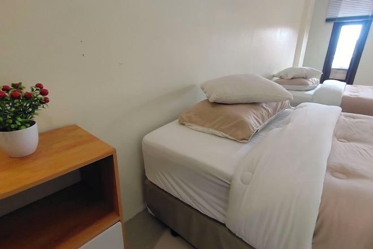 Une chambre à coucher avec un lit, des oreillers, une table de chevet et une plante en pot.