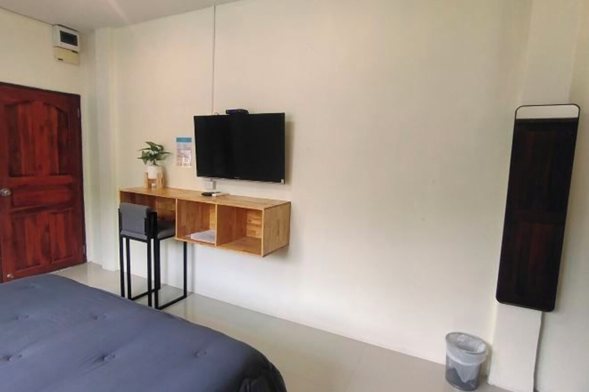 Une chambre à coucher avec un lit, un bureau et une chaise, une télévision et une poubelle.