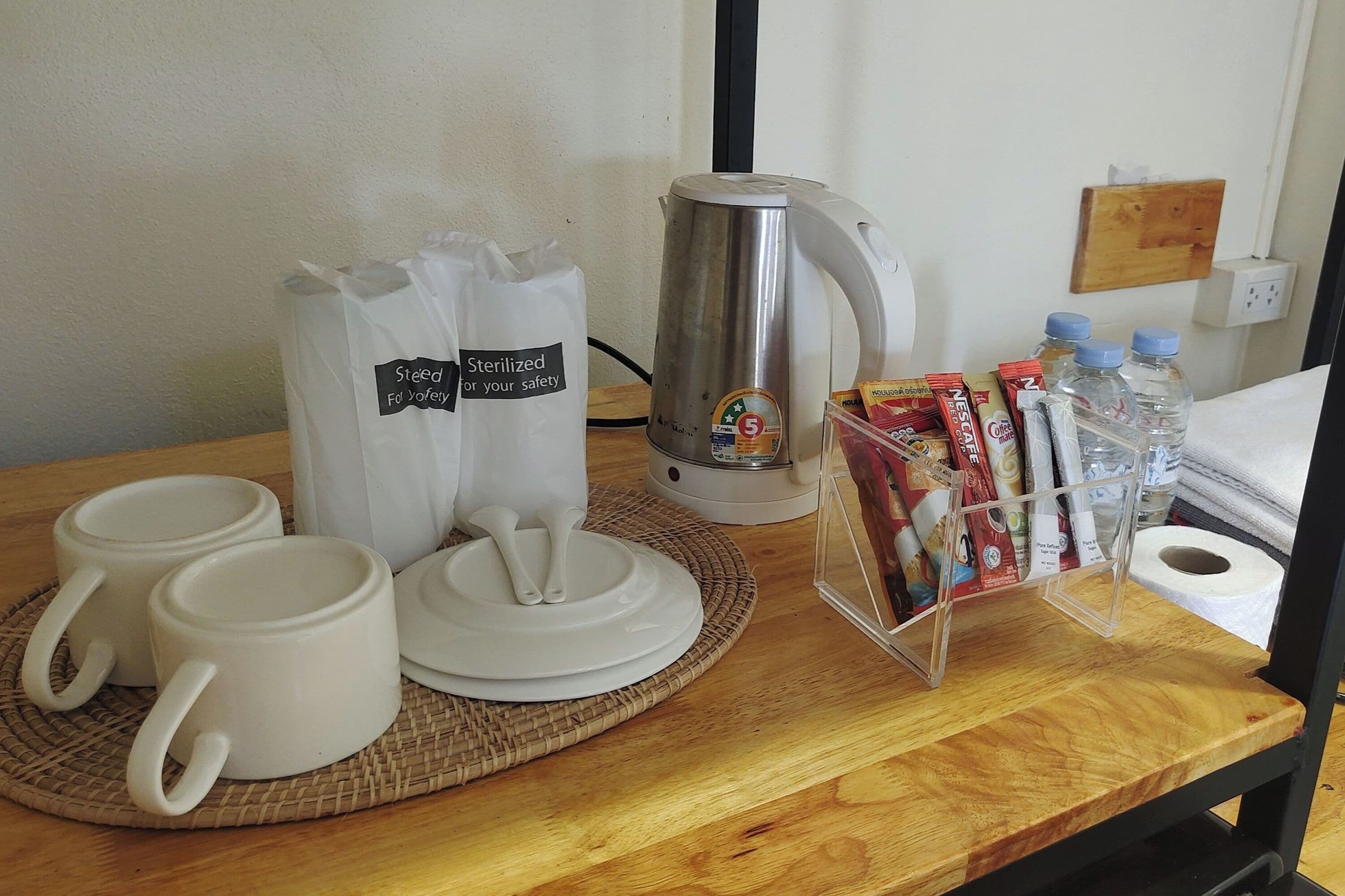 A breakfast setup with two white mugs, a coffee maker, a water dispenser, and a magazine rack with various items.