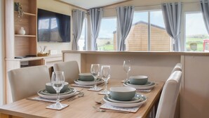 A dining area with a table set for four, chairs, a television, and a window with curtains. - 2 bedroom accommodation in Moota, near Cockermouth (Moota, near Cockermouth)