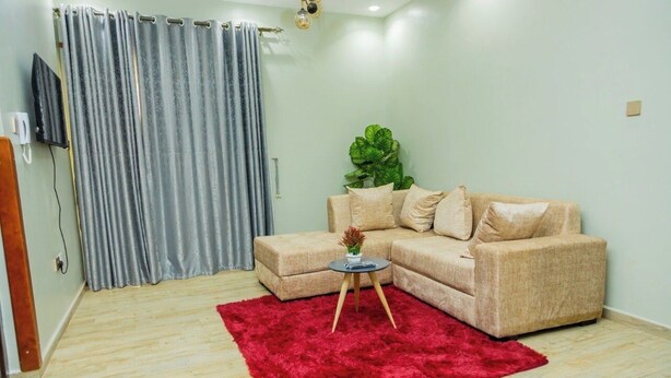 Ein Wohnzimmer mit einem beigen Sofa, einem roten Teppich und einer Pflanze.