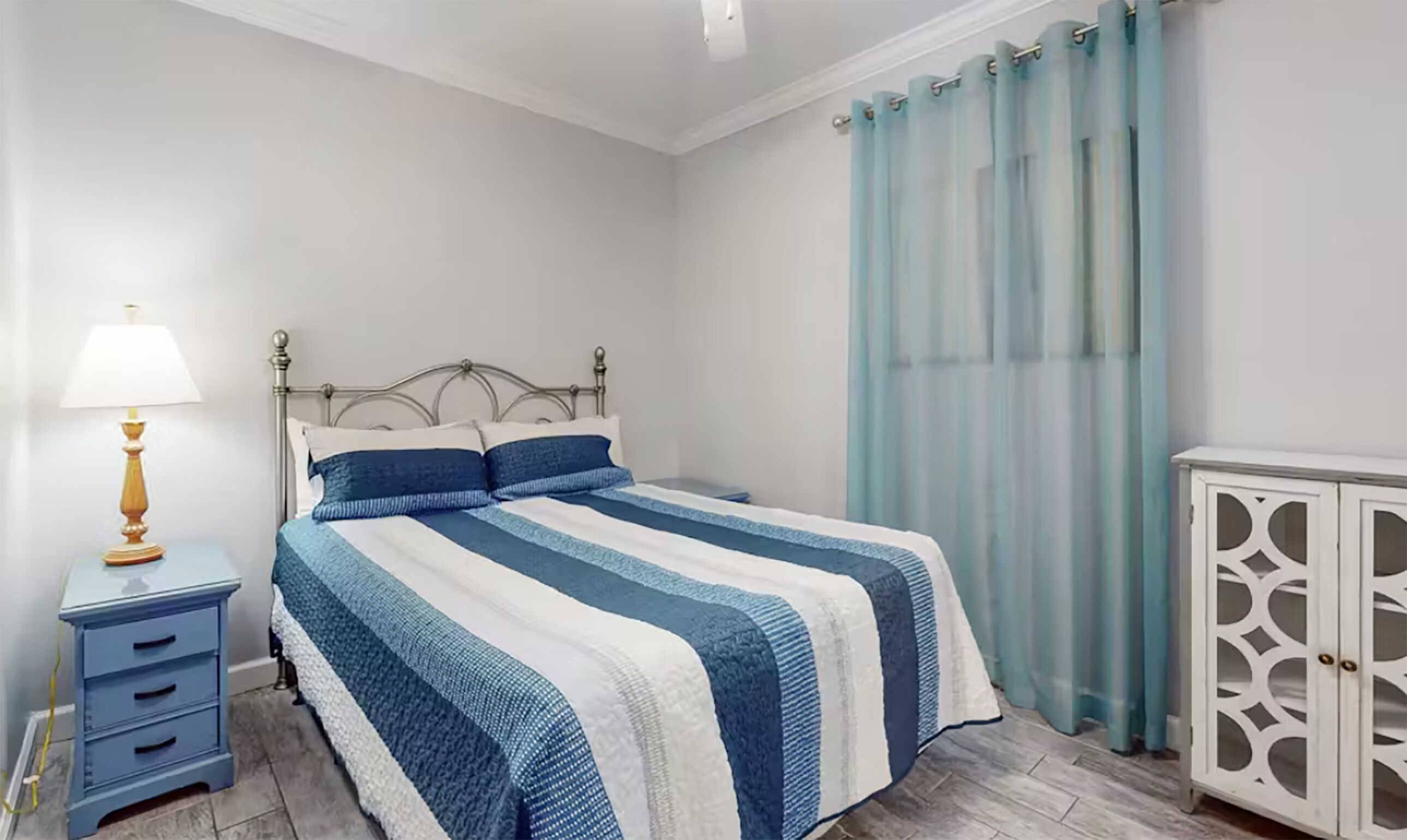 A neatly arranged bedroom with a bed, a bedside table with a lamp, a wardrobe, and a window with curtains.