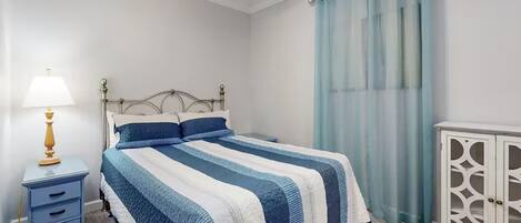 A neatly arranged bedroom with a bed, a bedside table with a lamp, a wardrobe, and a window with curtains.