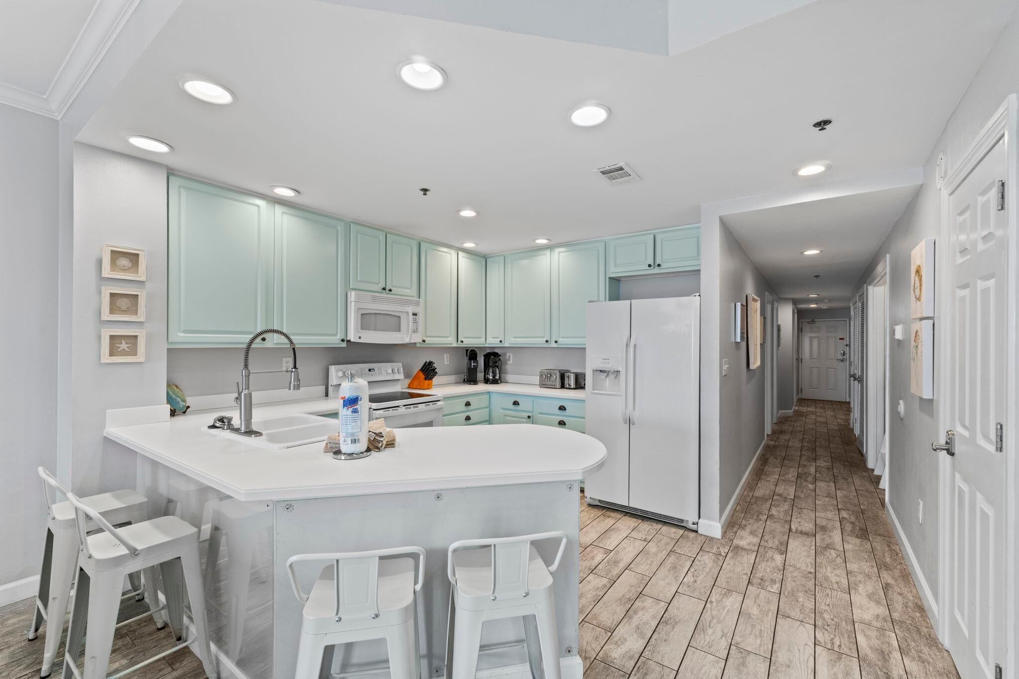 A modern kitchen with white countertops, teal cabinets, and a central island with bar stools.