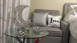 Et hyggeligt soveværelse med et glas-sofabord, en grå sofa og dekorative puder, herunder en pude med teksten "Love".