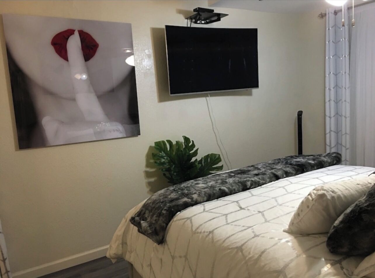A bedroom with a bed, a TV mounted on the wall, and a large painting.