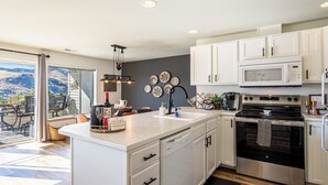 A modern kitchen with white cabinets, a stainless steel oven, and a large island with a sink. - Chelan Condo | Breathtaking Mountain & Lake Views (Chelan)
