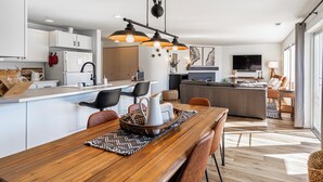 A modern kitchen with white cabinets, a dining area with a wooden table, and a living room with a sofa and TV. - Chelan Condo | Breathtaking Mountain & Lake Views (Chelan)